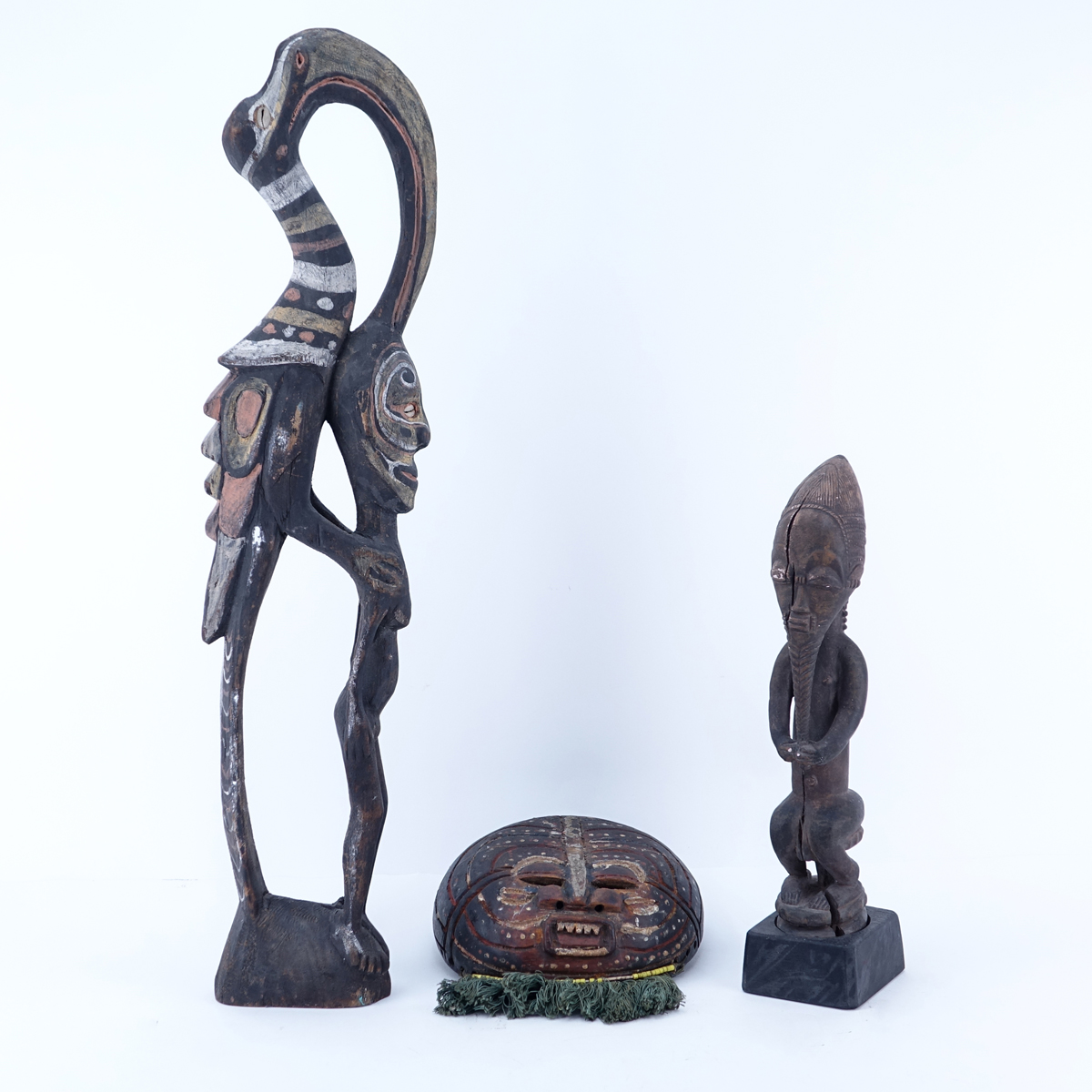 Antique Tribal Grouping of Three (3): African Polychrome Hornbill Bird with Figure, African Round Carved Wood Mask, and Possibly Dayak Carved Seated Male Figure. All figures are in antique condition, splits and chips.