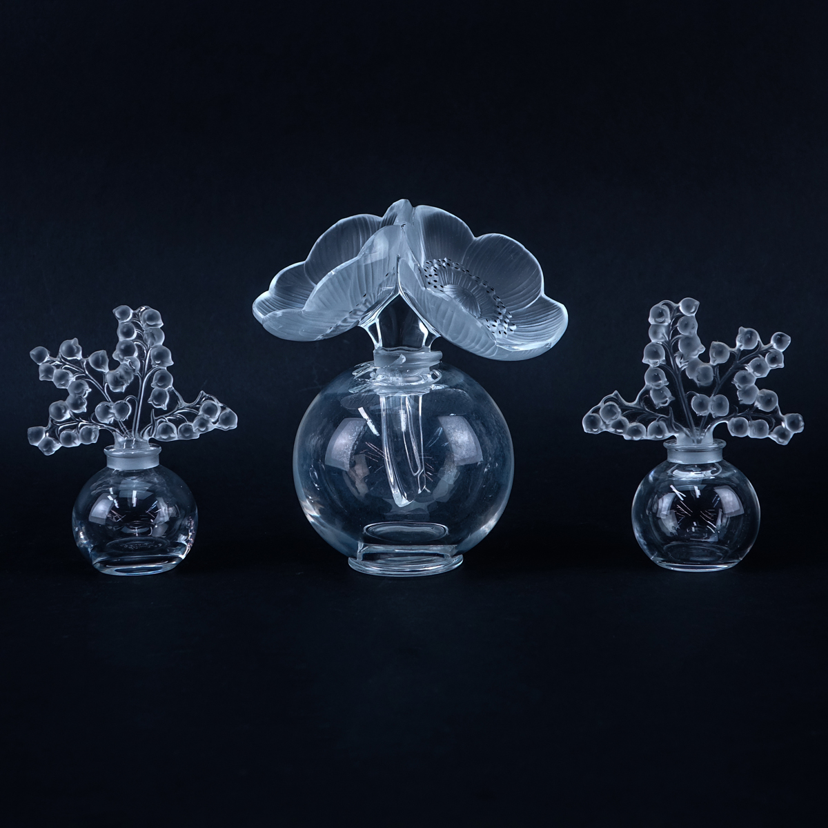 Group of Three (3): Pair of Lalique "Lily of the Valley" Crystal Perfume Bottles, Large Lalique "Anemone" Crystal Perfume Bottle. Each appropriately signed to base.